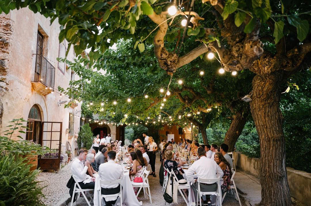 Long outdoor dinner table beneath mature trees at Halley and Dani’s Sitges wedding