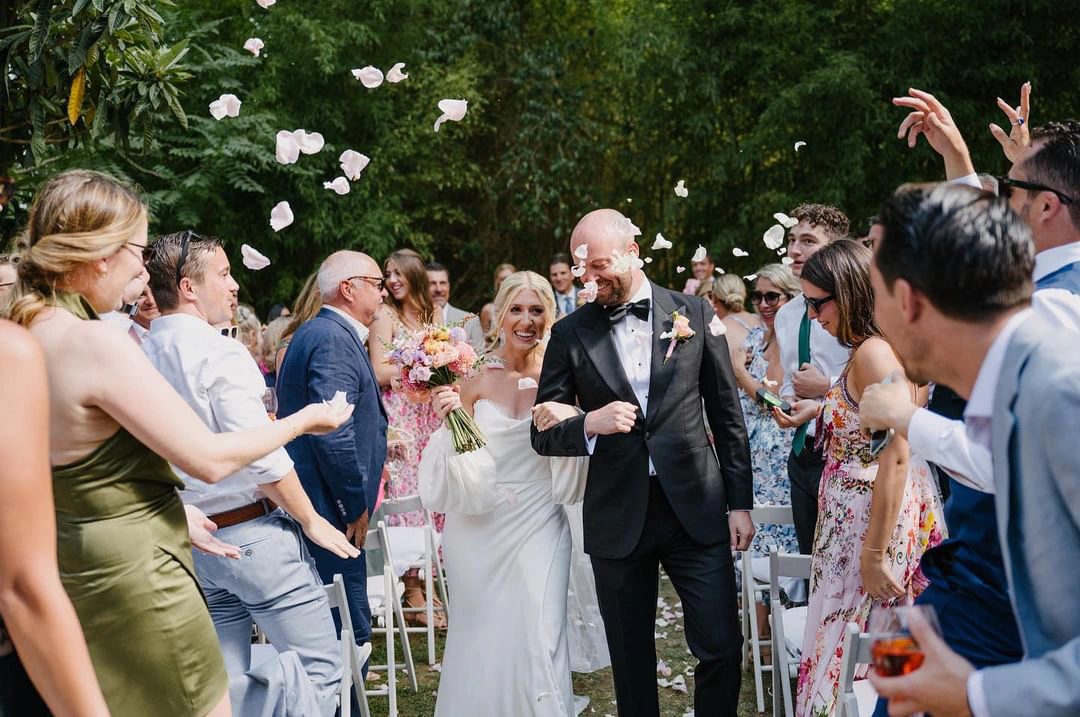 Halley and Dani leaving their courtyard ceremony in Sitges as guests celebrate